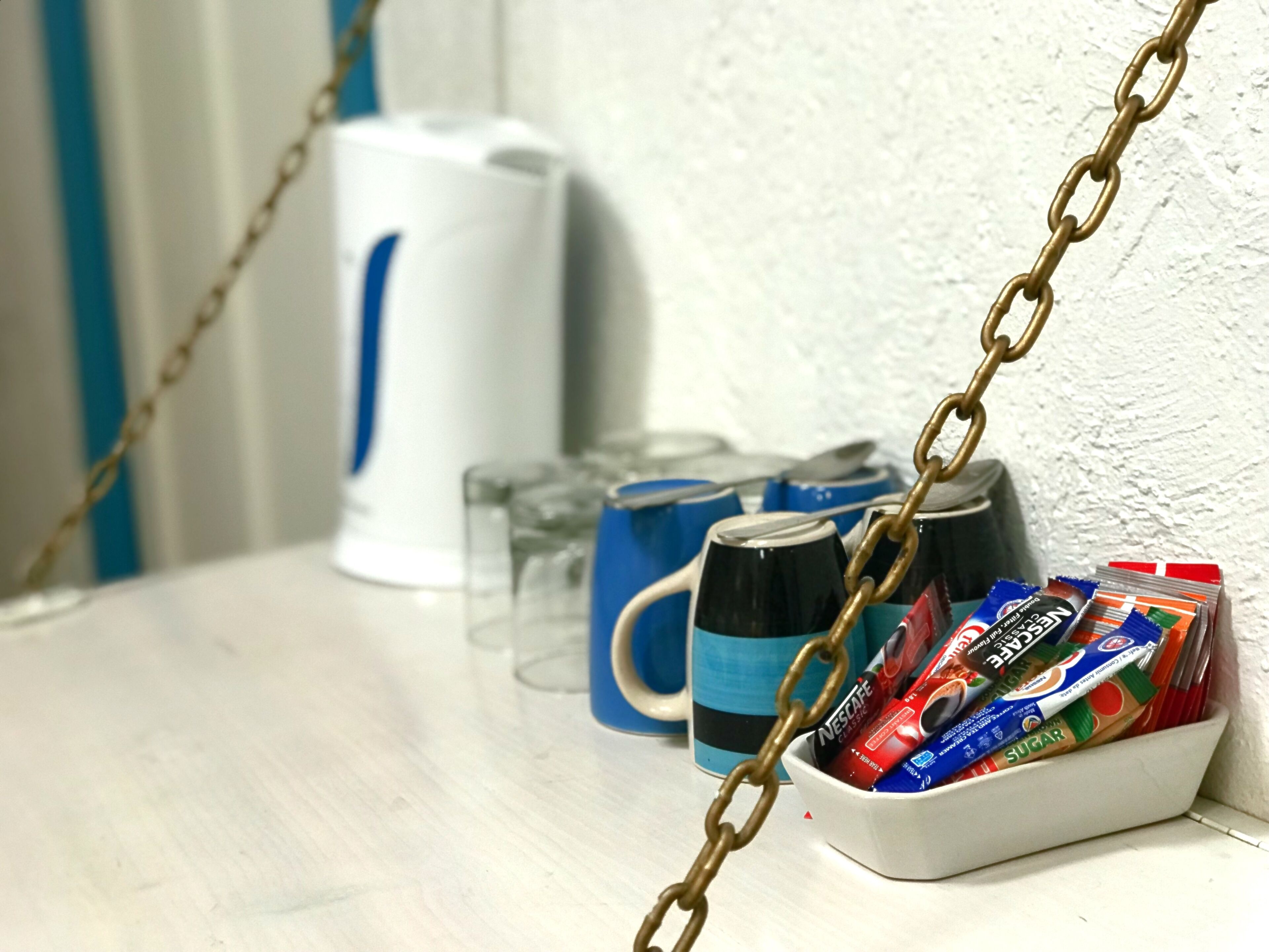 A kitchen counter with a coffee maker, mugs, and a basket of snacks.