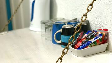 A kitchen counter with a coffee maker, mugs, and a basket of snacks.