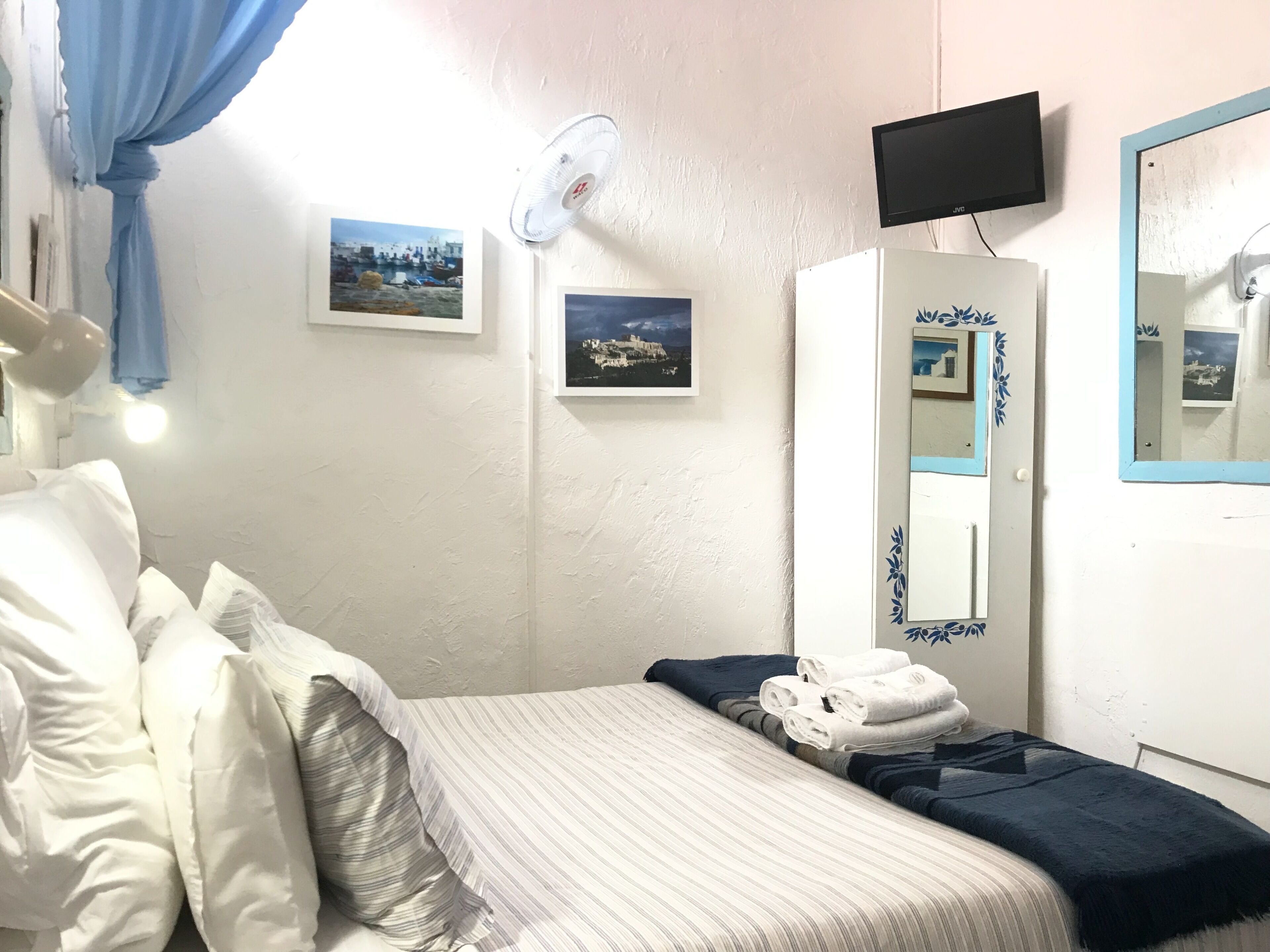 Hotellihuone, jossa on sänky, vaatekaappi, televisio ja kaksi kehystettyä kuvaa seinällä.