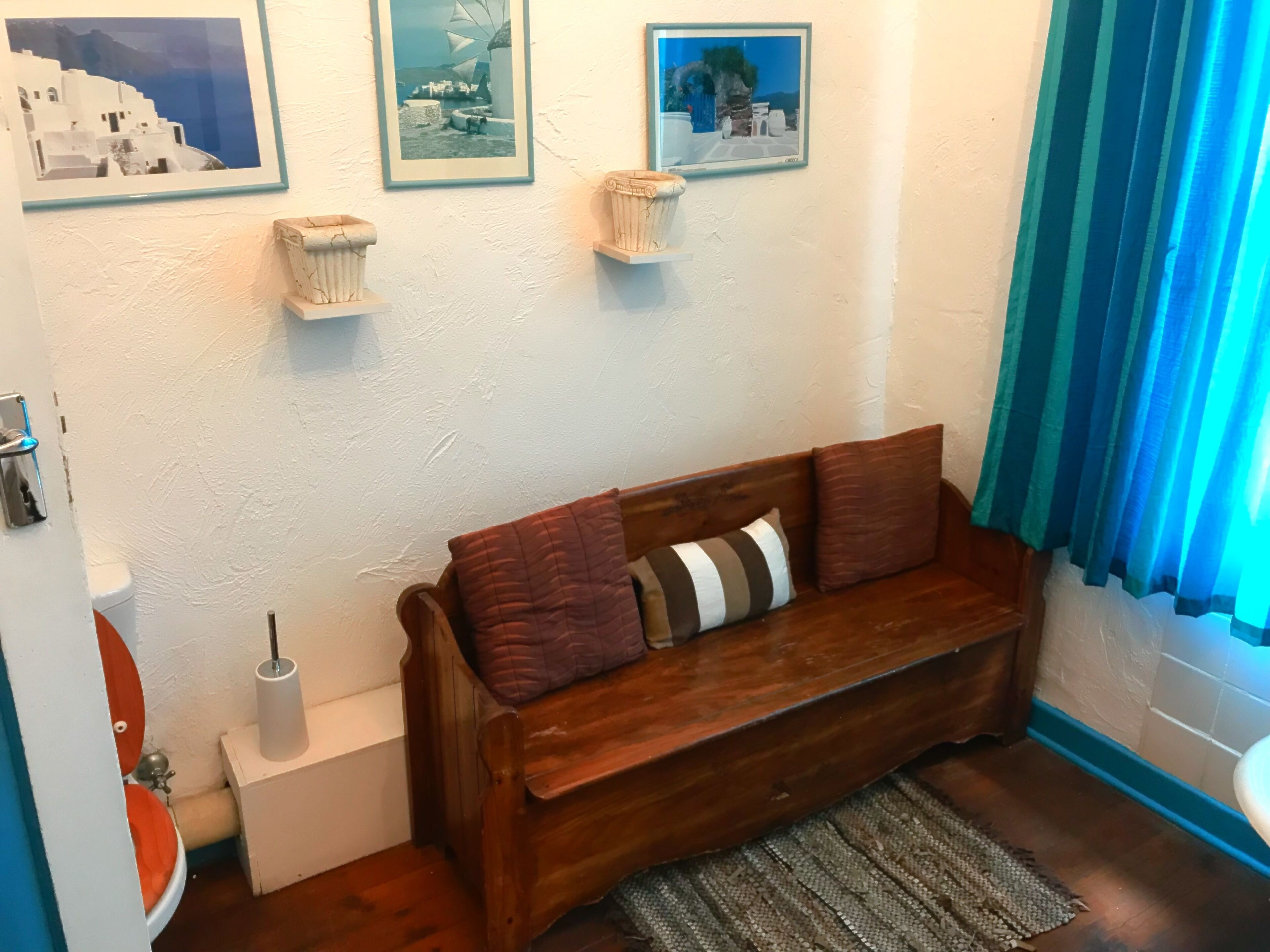 A wooden bench with cushions, a small white shelf, and a framed picture on the wall.