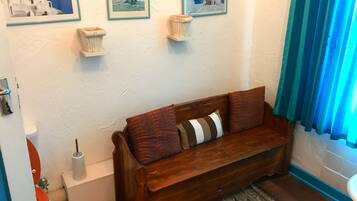A wooden bench with cushions, a small white shelf, and a framed picture on the wall.