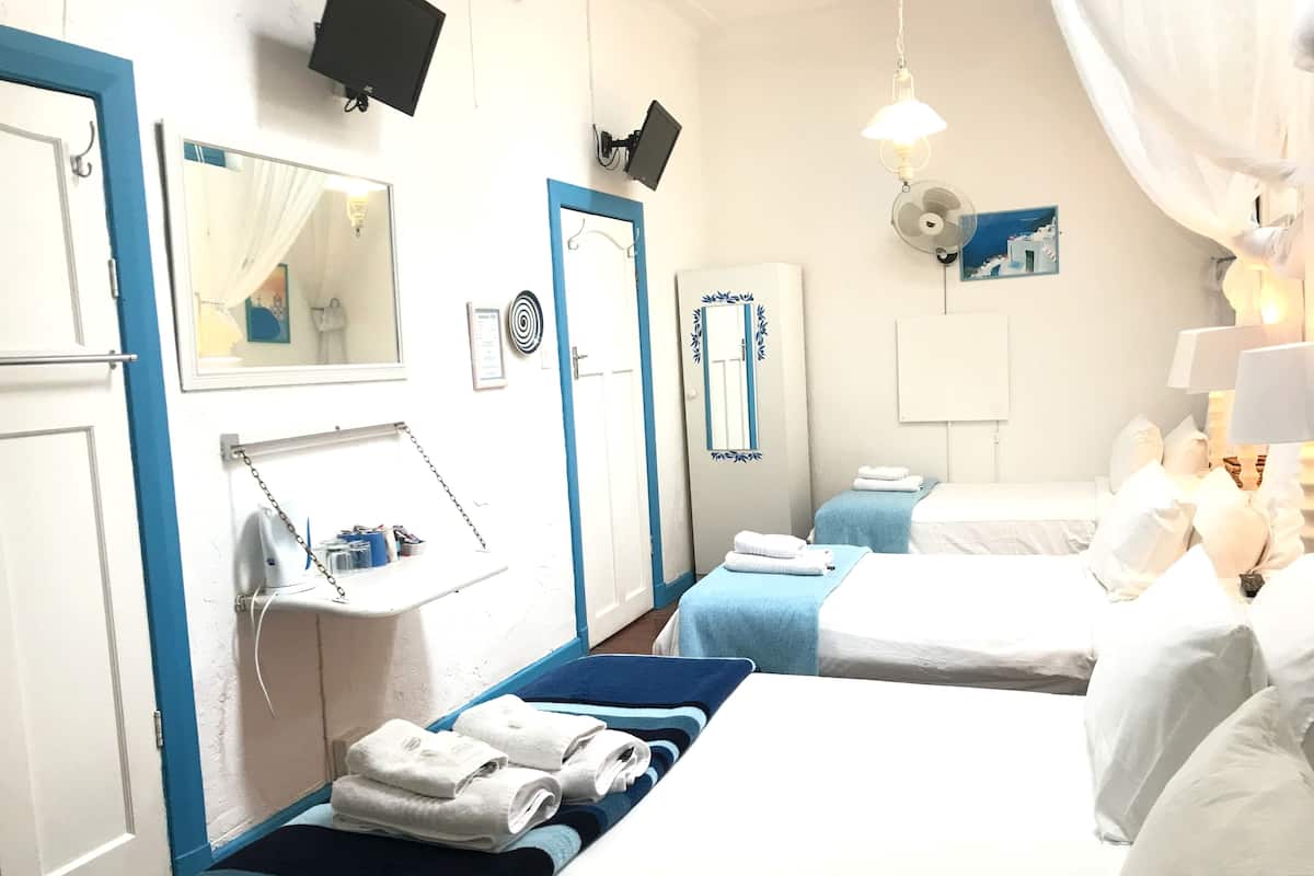 A hotel room with two beds, a small desk with a mirror, a wall-mounted TV, and a ceiling fan.