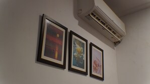 Trois œuvres d’art encadrées sont accrochées à un mur, juste en dessous d’un appareil de climatisation.