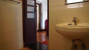 Une salle de bain avec un lavabo blanc, une porte dotée de panneaux en verre dépoli et un tapis rouge à l’entrée.