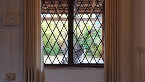 Une fenêtre avec une grille métallique, un fauteuil suspendu et une vue sur la verdure à l’extérieur.