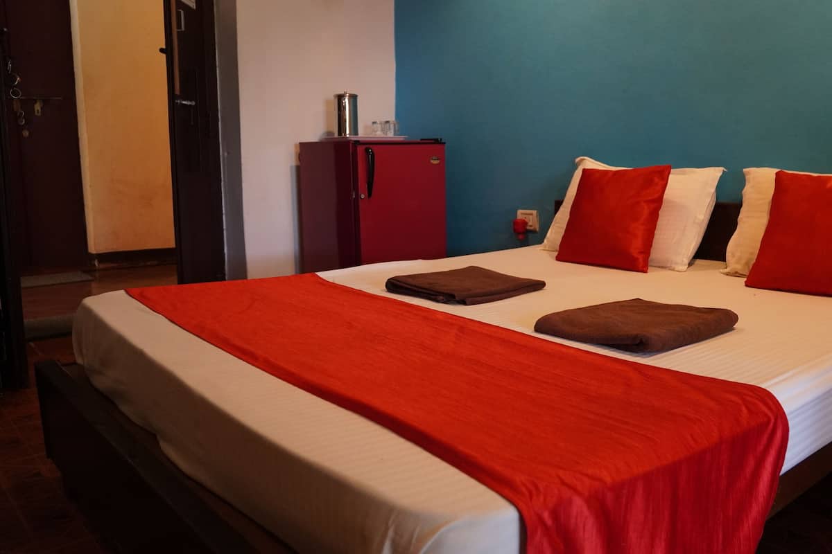 A hotel room with a bed, red and white pillows, a red blanket, and a minibar.