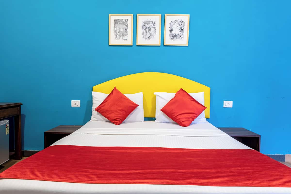A bed with a yellow headboard, red and white bedding, and two red pillows. There are three framed pictures on the wall above the bed.