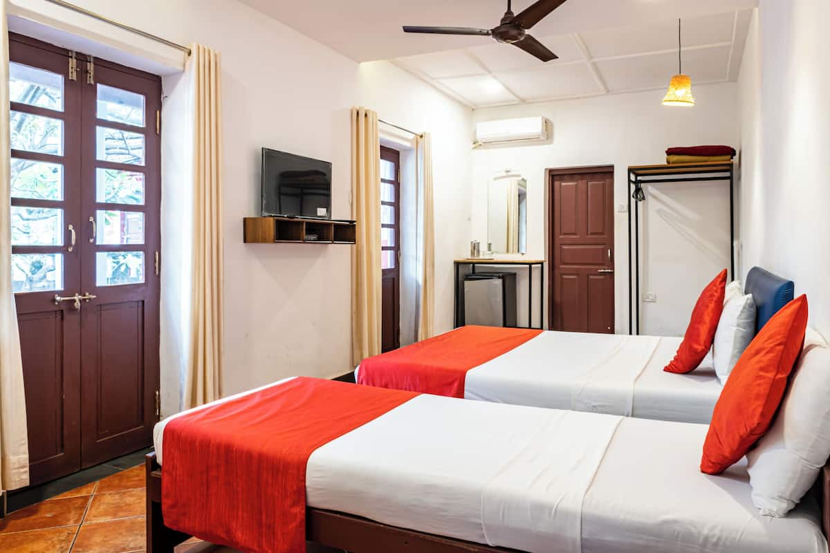 A hotel room with two beds, a ceiling fan, a TV, and a wardrobe.