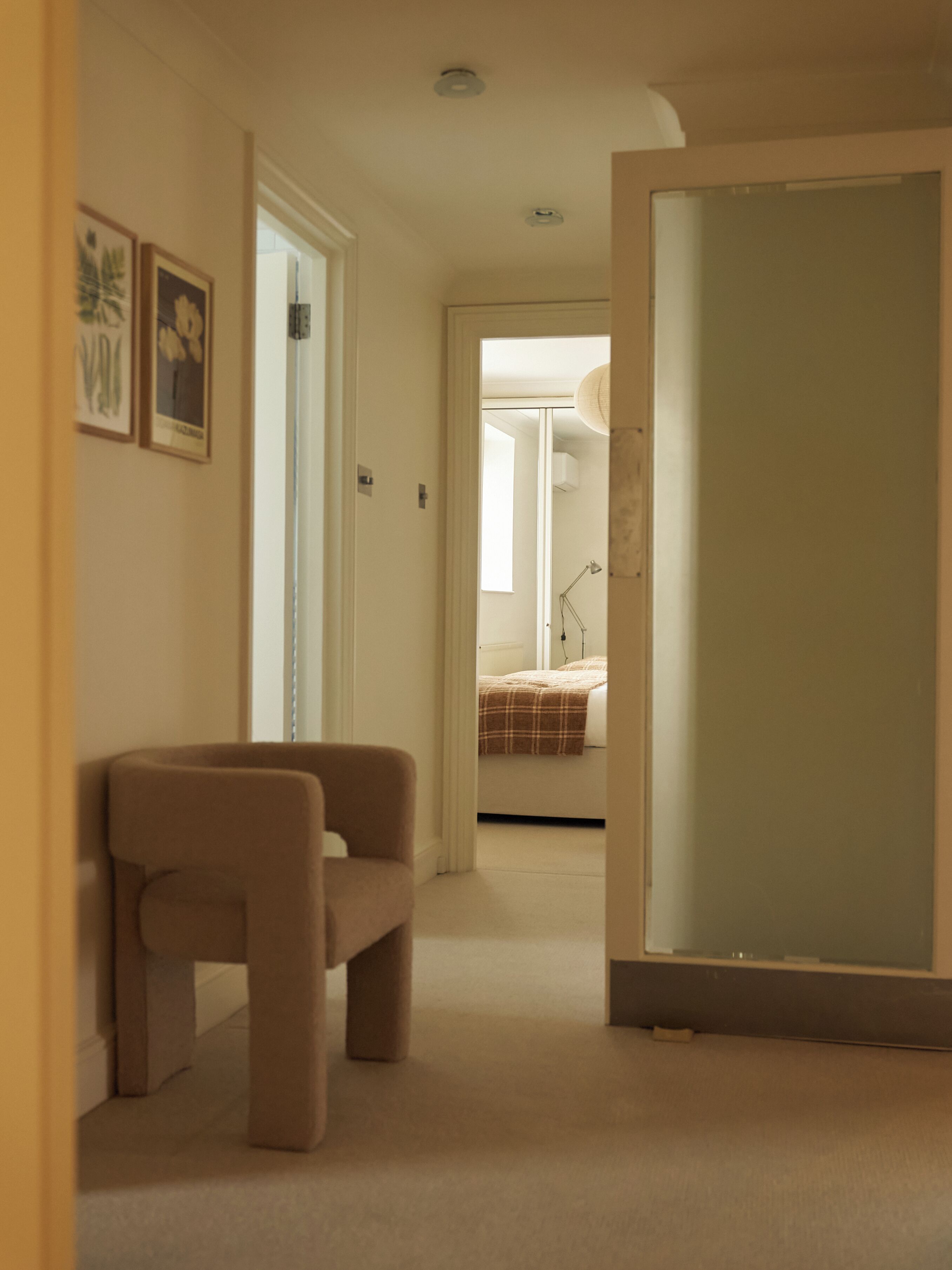 Un couloir avec un tapis beige, une chaise marron et un lit à l’arrière-plan.