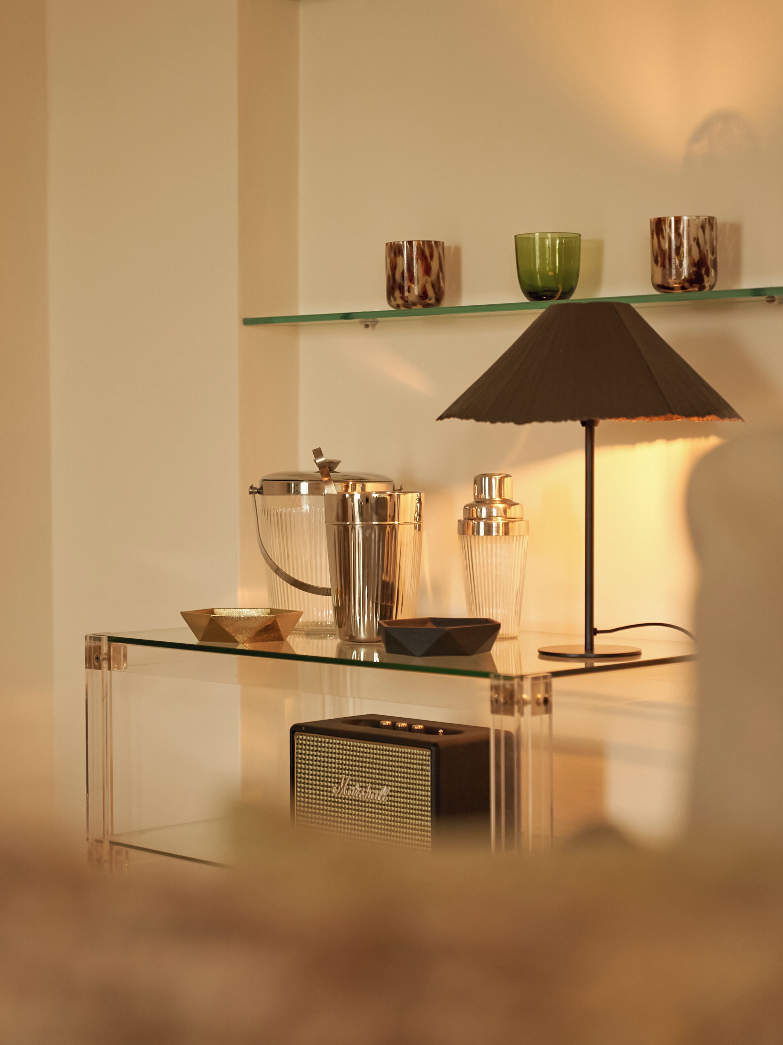 A modern interior with a glass table displaying a radio, a lamp, and decorative items.