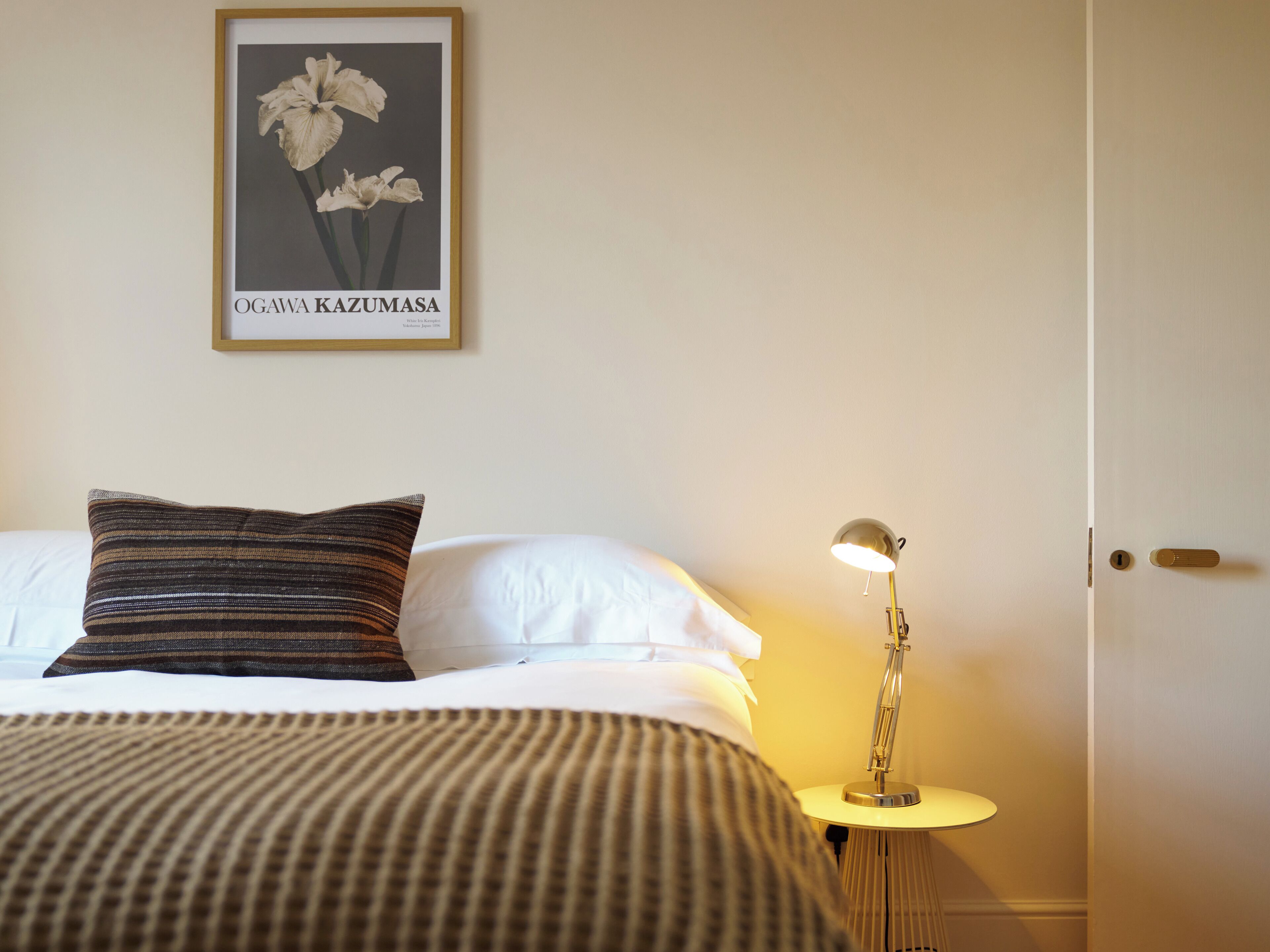 Habitación de hotel con cama, almohada, mesita de noche con lámpara y un cuadro en la pared.