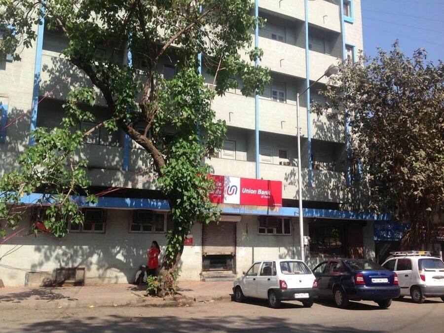 Un edificio con un letrero rojo del Union Bank, coches estacionados y un árbol en la parte delantera.