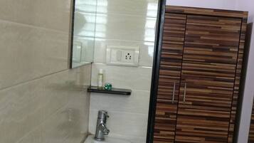 A bathroom with a white sink, a mirror, a towel rack, and a wooden wardrobe.