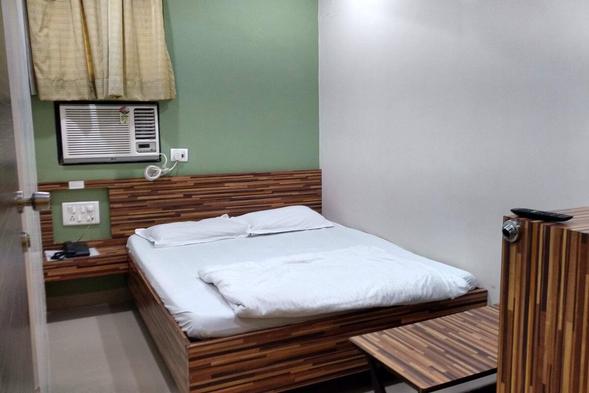 Una stanza piccola e ordinata con un letto in legno, un comodino e un condizionatore d'aria a parete.