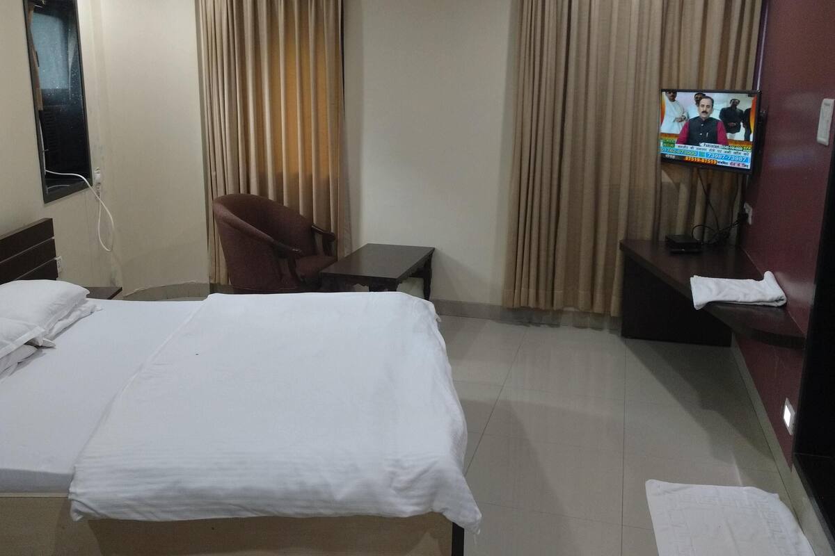 Una camera d'albergo con un letto, una sedia, un tavolino e una televisione appesa al muro.