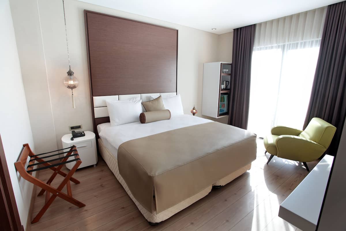Une chambre d’hôtel moderne avec un grand lit, une table de chevet, une lampe, une chaise et une armoire.