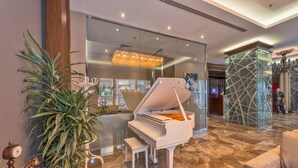 Um piano de cauda em um hall moderno com piso de mármore, uma grande planta em vaso e um candelabro.