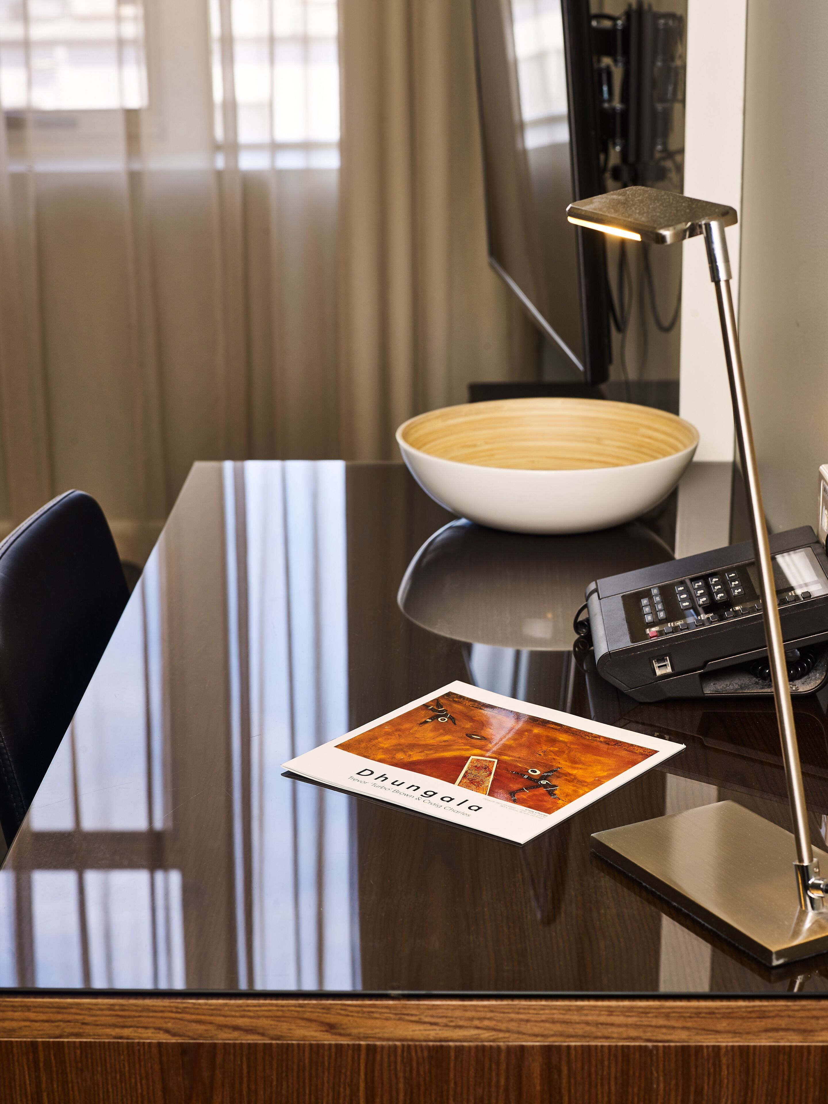 A hotel room with a wooden desk, a bowl, a telephone, and a lamp.