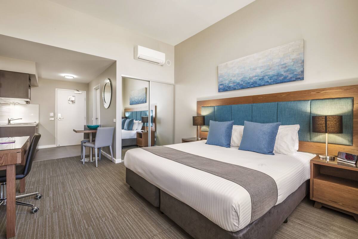Quarto de hotel com uma cama grande, uma escrivaninha, uma cadeira, um espelho e um quadro na parede.