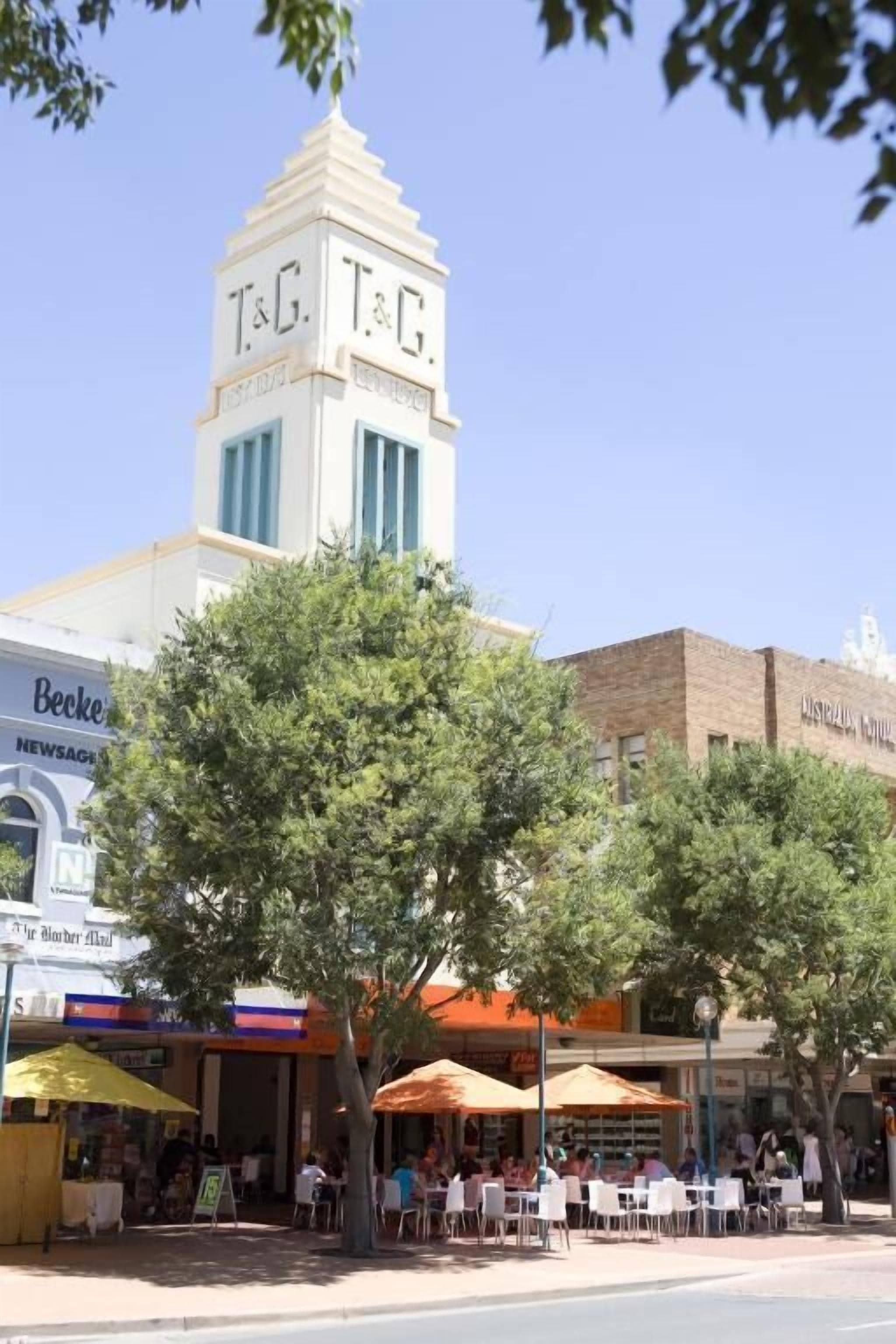 A building with a clock tower, outdoor seating, and various storefronts.