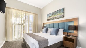 Habitación de hotel con una cama grande, una mesita de noche con lámpara, un cuadro en la pared y cortinas translúcidas en la ventana.
