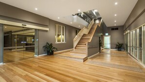 A spacious lobby with a wooden staircase, glass doors, and potted plants. - Quest Albury On Townsend (Albury)
