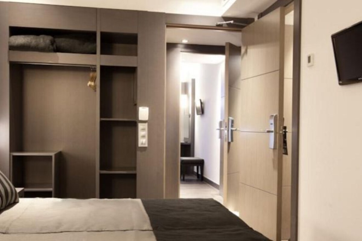Ett modernt hotellrum med en säng, en garderob och en tv.