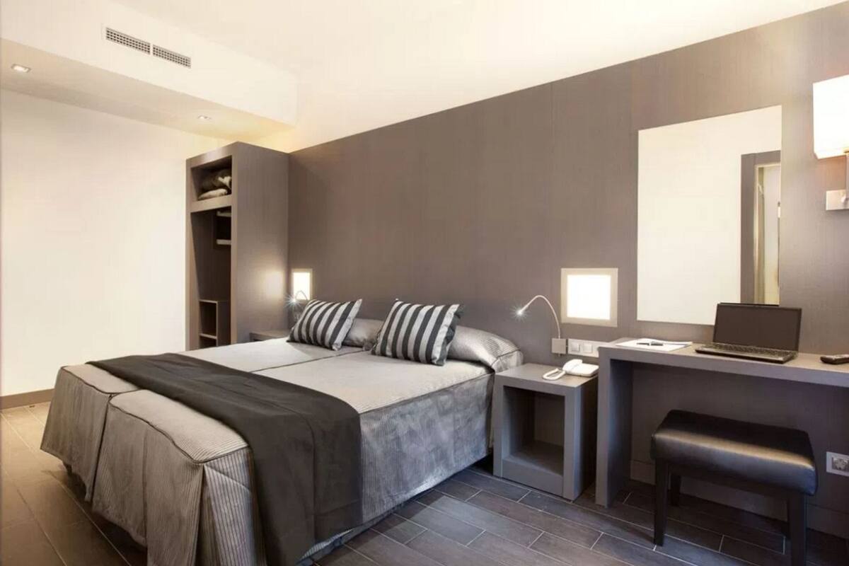 A modern hotel room with a bed, bedside table, desk, and chair.