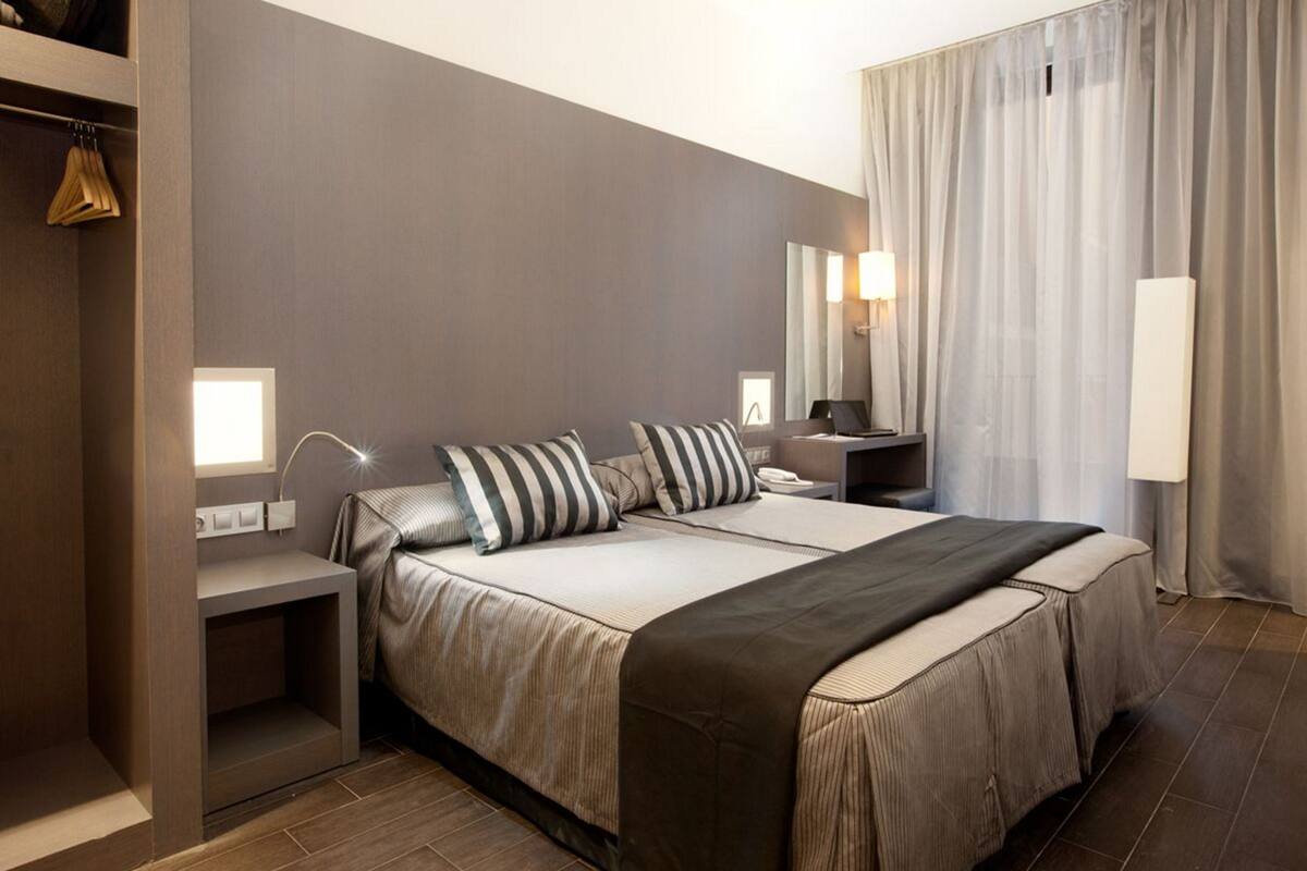 A modern hotel room with a large bed, bedside tables, a wardrobe, and a mirror.