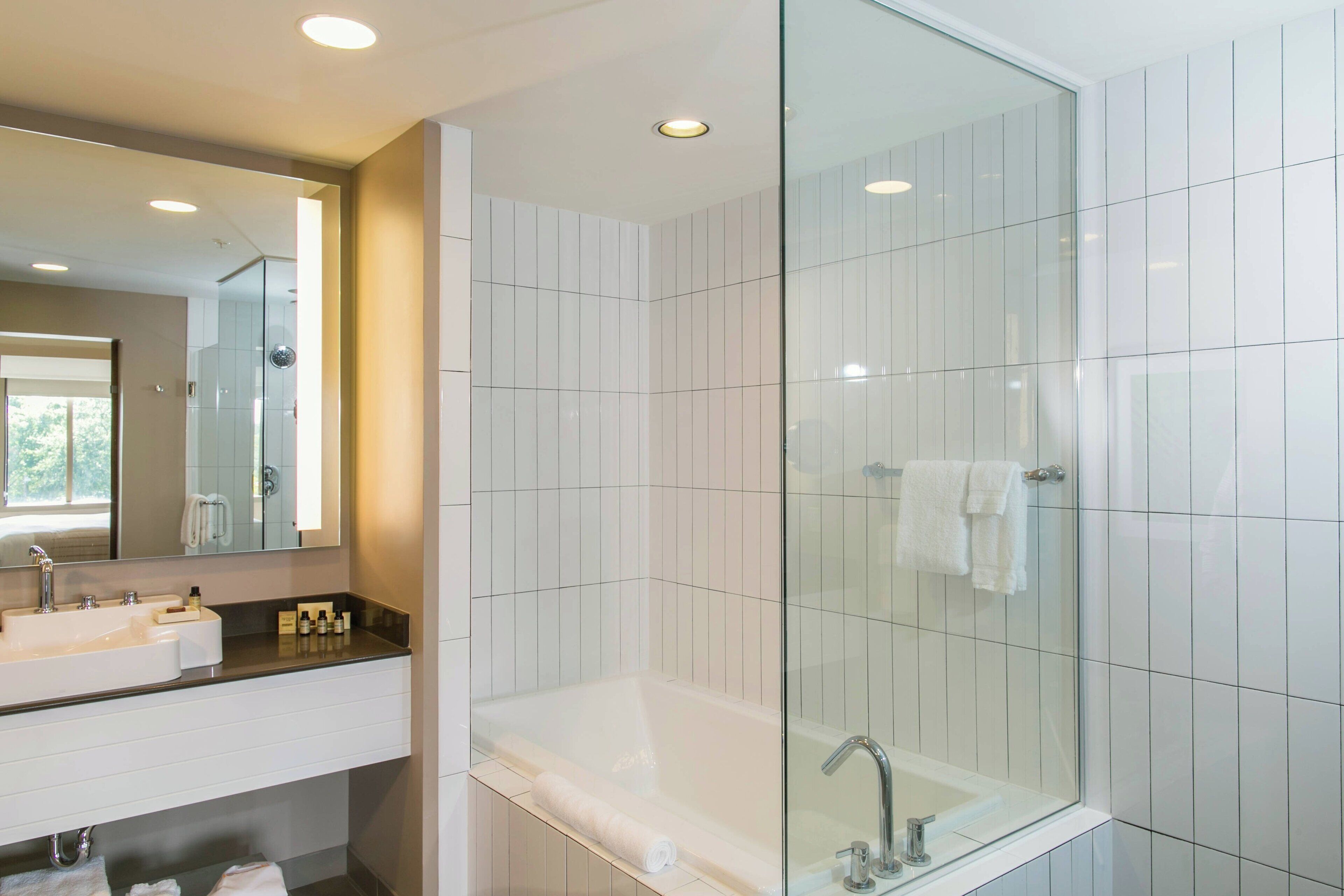 A modern bathroom with a glass-enclosed shower, a large bathtub, and a vanity with a sink and mirror.