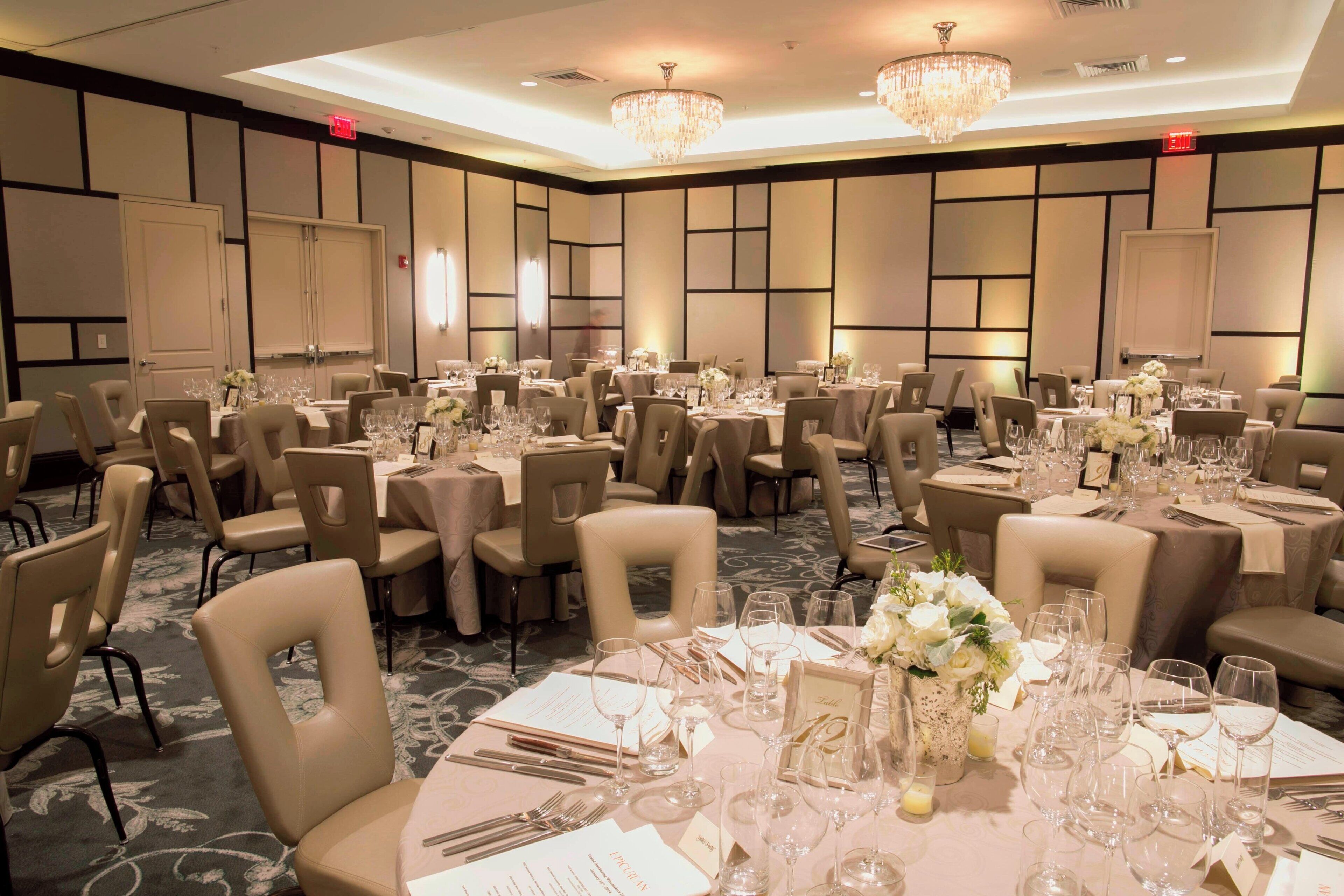 A banquet hall with multiple round tables set for dining, each with chairs, place settings, and floral centerpieces.
