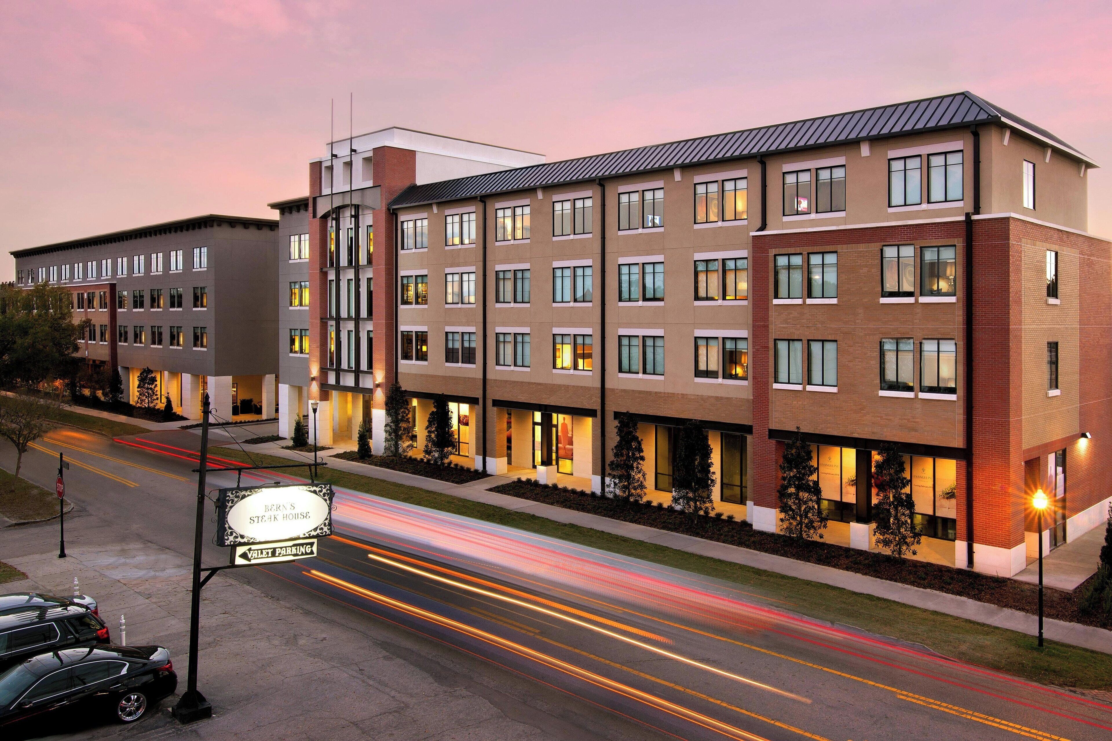 A multi-story hotel with a modern design, featuring a sign for a steakhouse, valet parking, and a well-lit entrance.