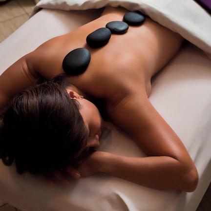 A person receiving a hot stone massage on a bed with a blanket.
