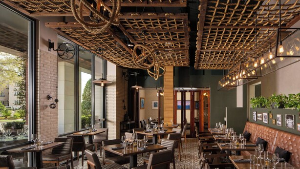 A restaurant with wooden tables and chairs, a patterned floor, and a ceiling with rope-like structures.