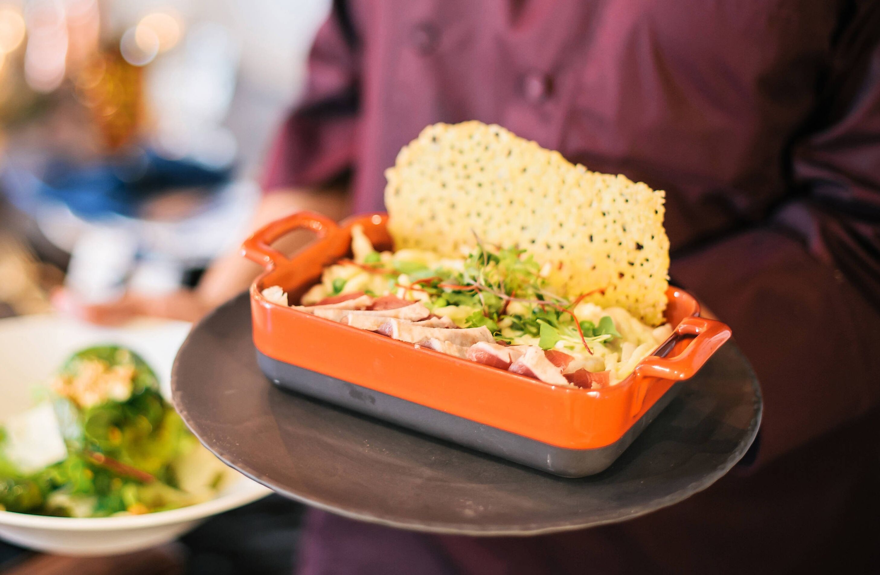 Une personne tenant une assiette avec de la viande et des légumes verts, et un biscuit sur une autre assiette.