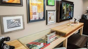 A room with a wooden desk, a glass display case with books, and various framed pictures on the wall.