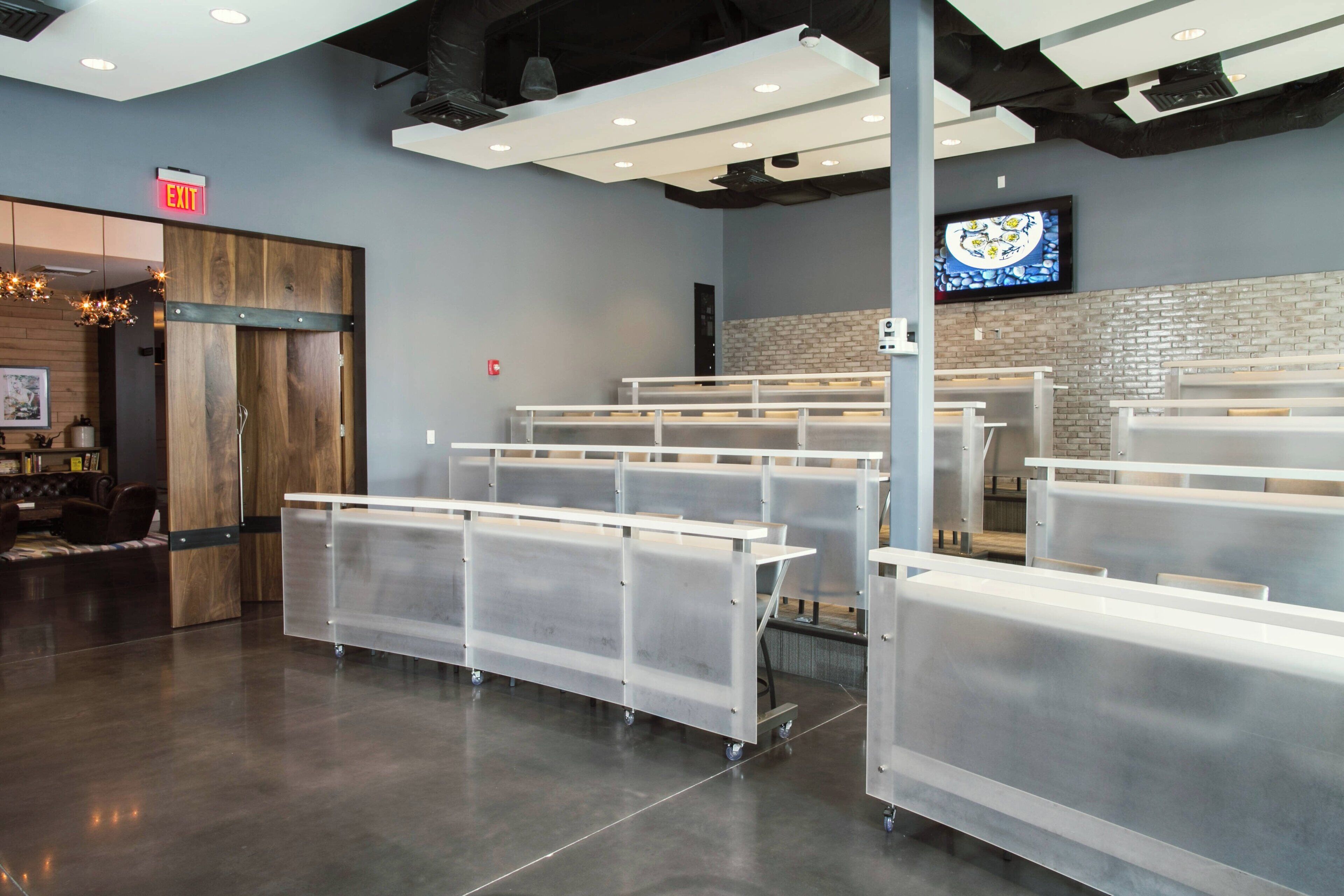 A modern restaurant interior with high tables and chairs, a brick wall, and a television screen.