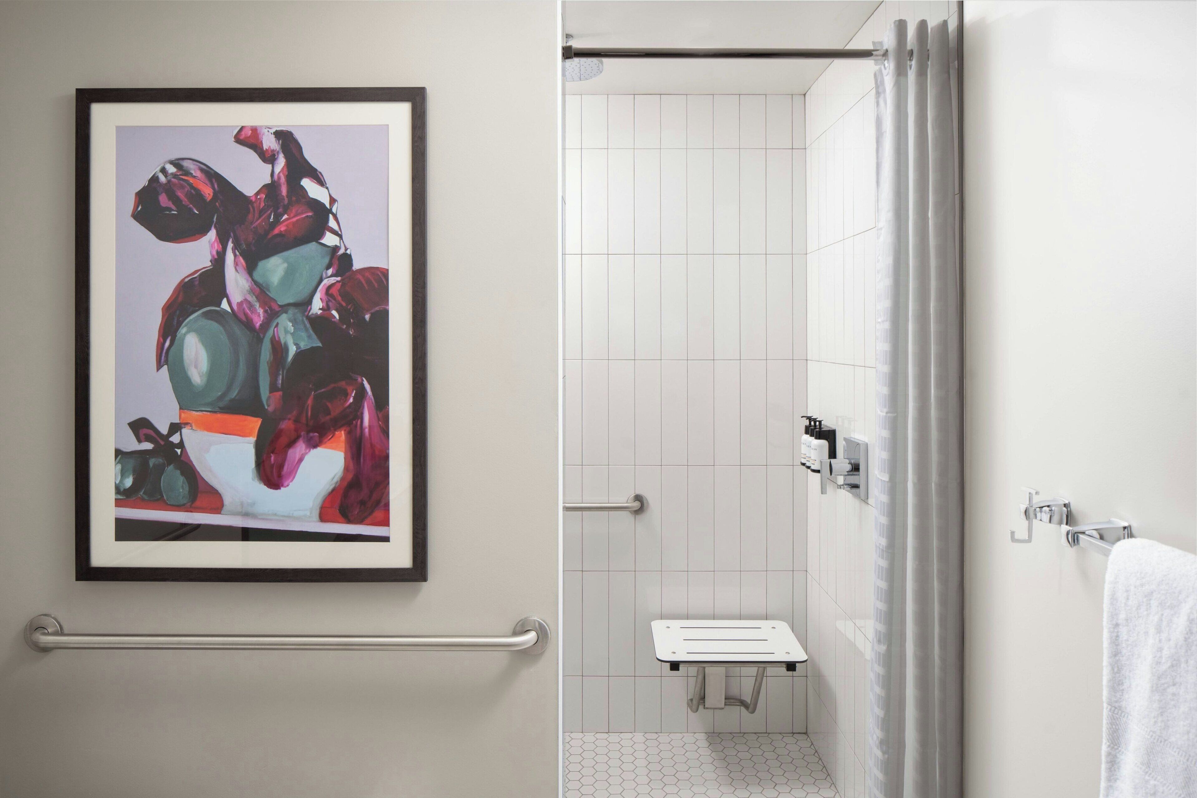 A bathroom with a shower, a framed artwork, a towel rack, and a handrail.