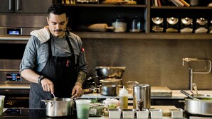 A chef in a kitchen with stainless steel appliances, a variety of cooking utensils, and ingredients on the counter.