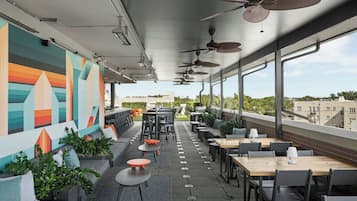An outdoor seating area with tables and chairs, ceiling fans, and a colorful mural on the wall.