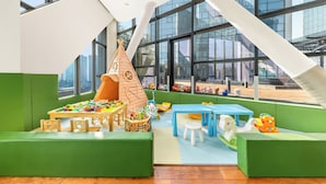 A children's play area with green seating, a play table, and a large window overlooking a cityscape. - Ascott Raffles City Chengdu (Chengdu)