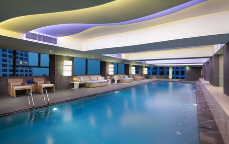 A modern indoor swimming pool with lounge seating and a view of the cityscape.