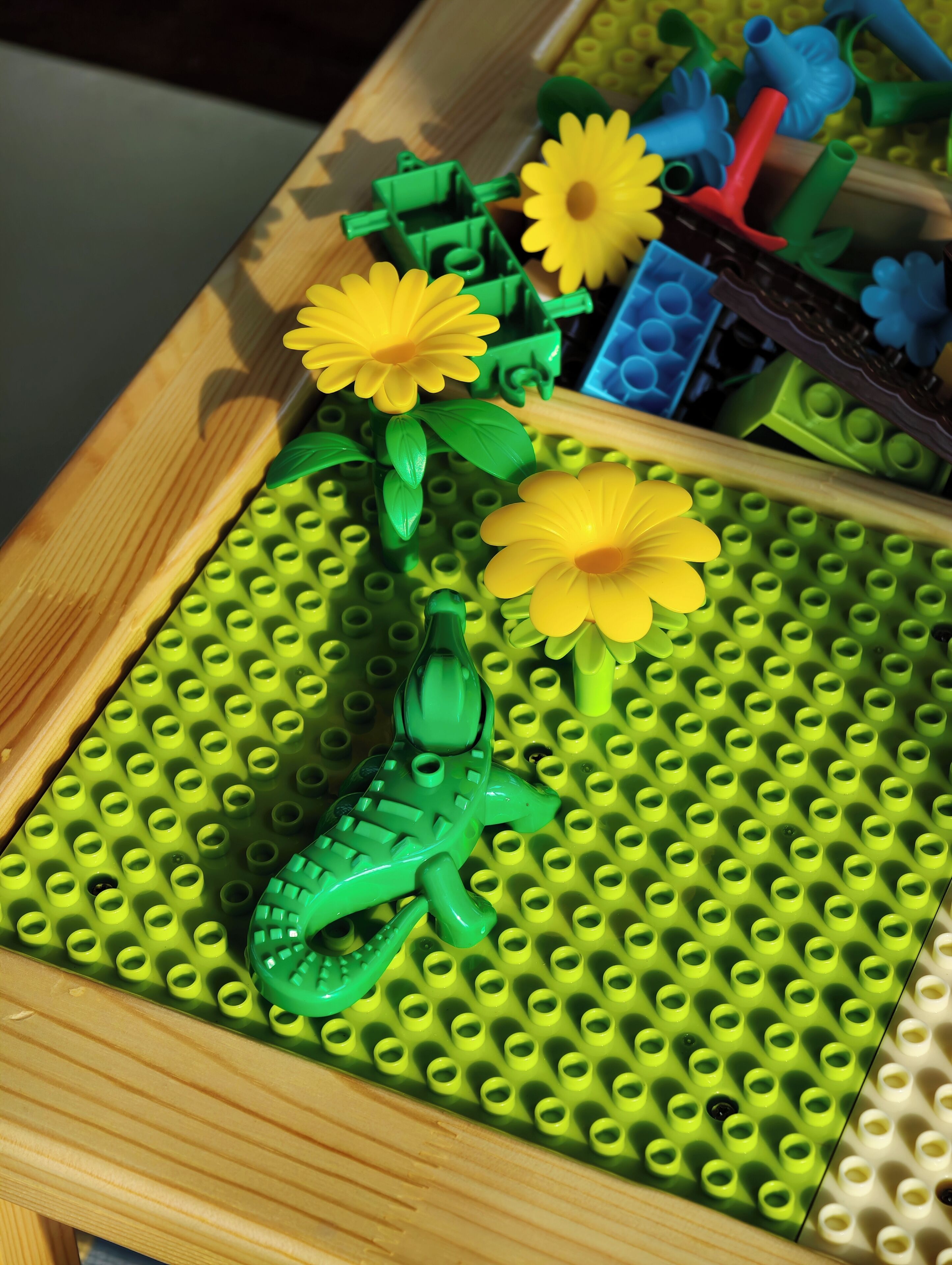 Ein LEGO-Set mit einem grünen Krokodil und gelben Blumen auf einer grünen Grundplatte.