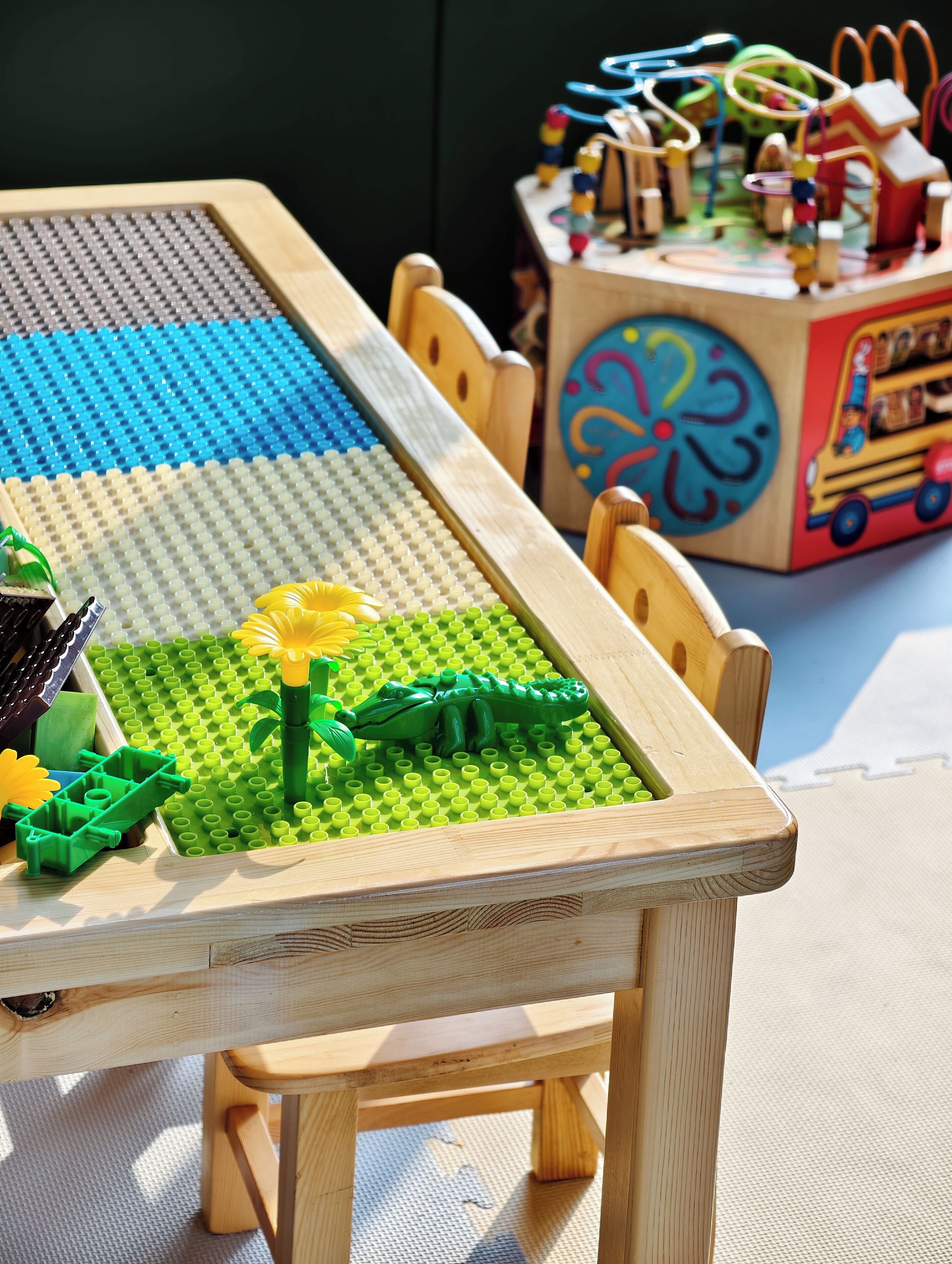 Una mesa de madera con un tapete de juego LEGO que muestra un dinosaurio y flores.