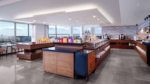 A modern cafe with a central counter, open shelving with various items, and a view of the city through large windows. - Ascott Raffles City Chengdu (Chengdu)
