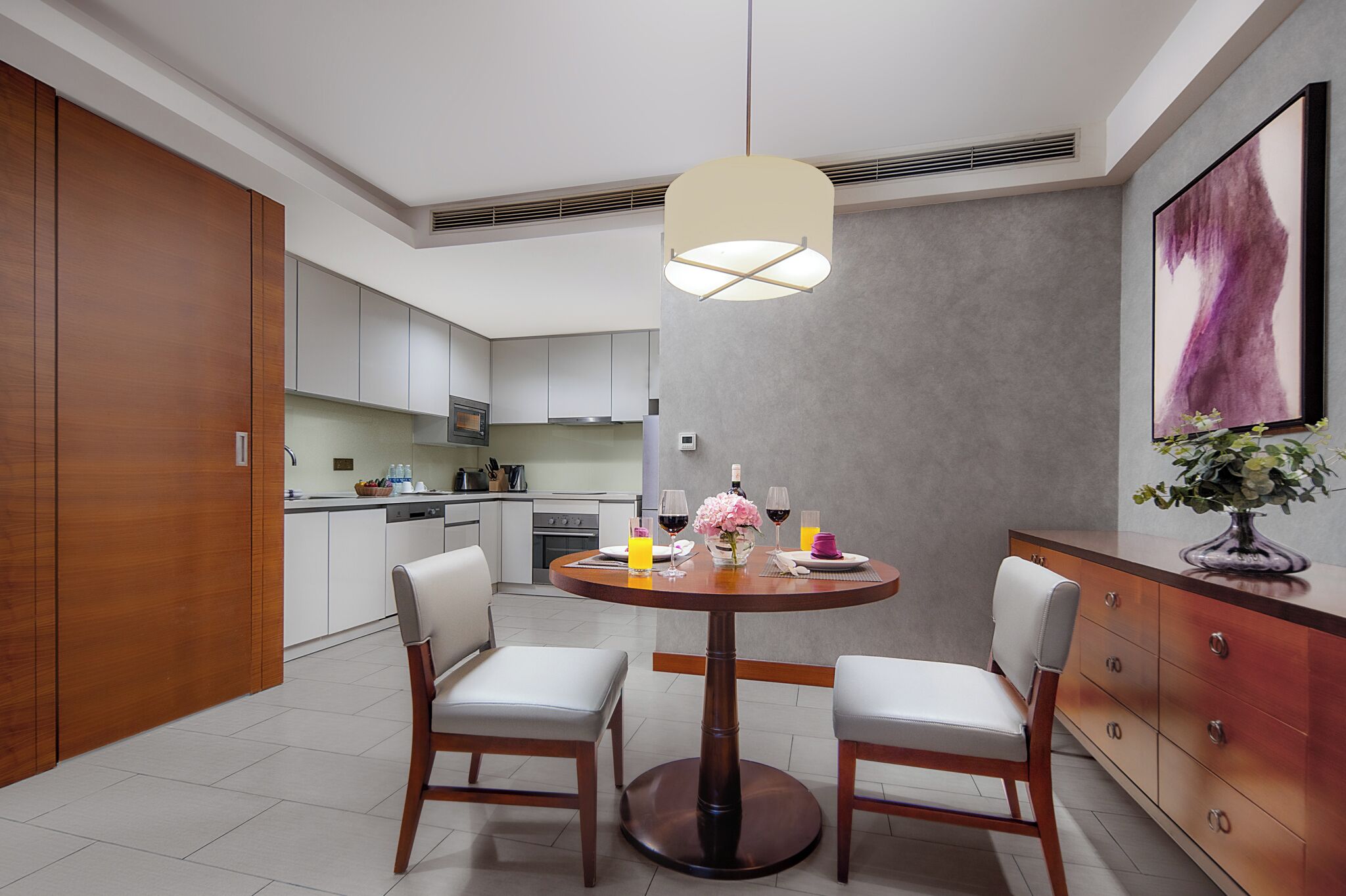 Une cuisine moderne avec des meubles blancs, un coin repas doté d’une table ronde et de chaises, et un luminaire suspendu.