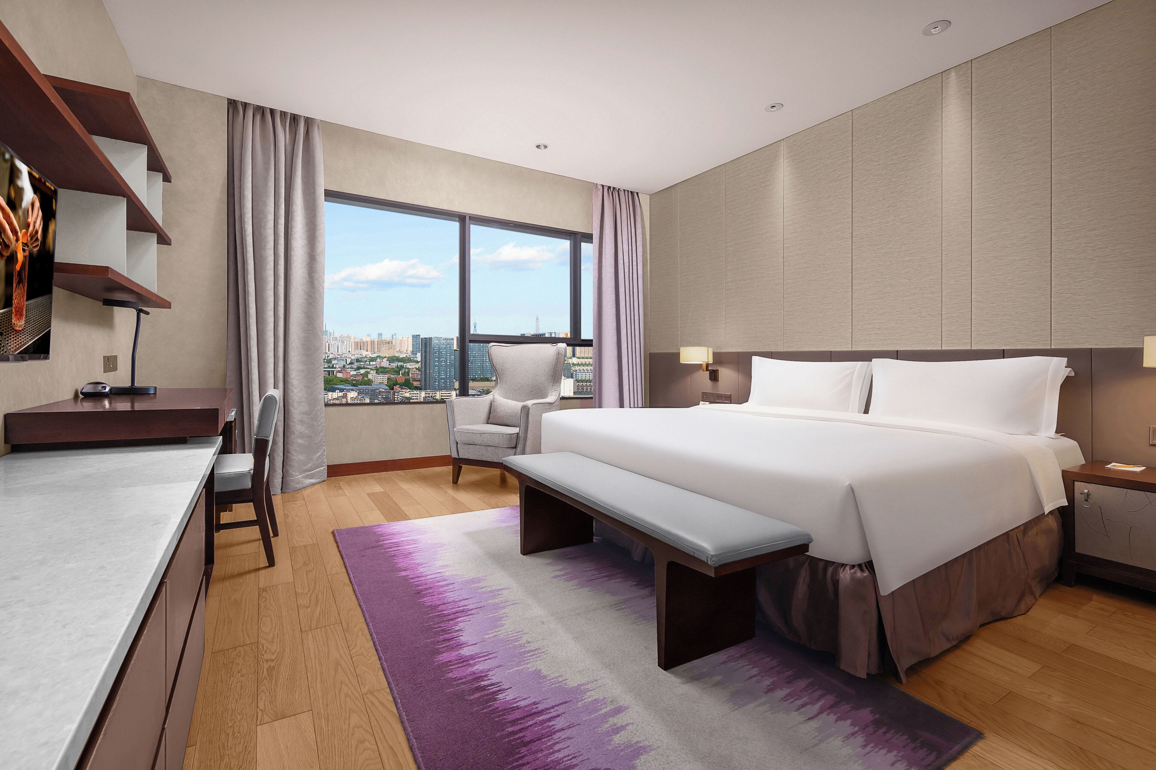 Habitación de hotel moderna con una cama grande, un escritorio y una silla. Se ve una vista de la ciudad a través de la ventana.