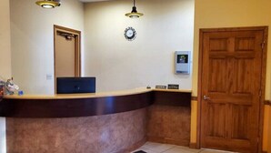 A reception area with a wooden reception desk, two pendant lights, a clock, a door, and a small sign. - Budget Inn Williamsport (Williamsport)