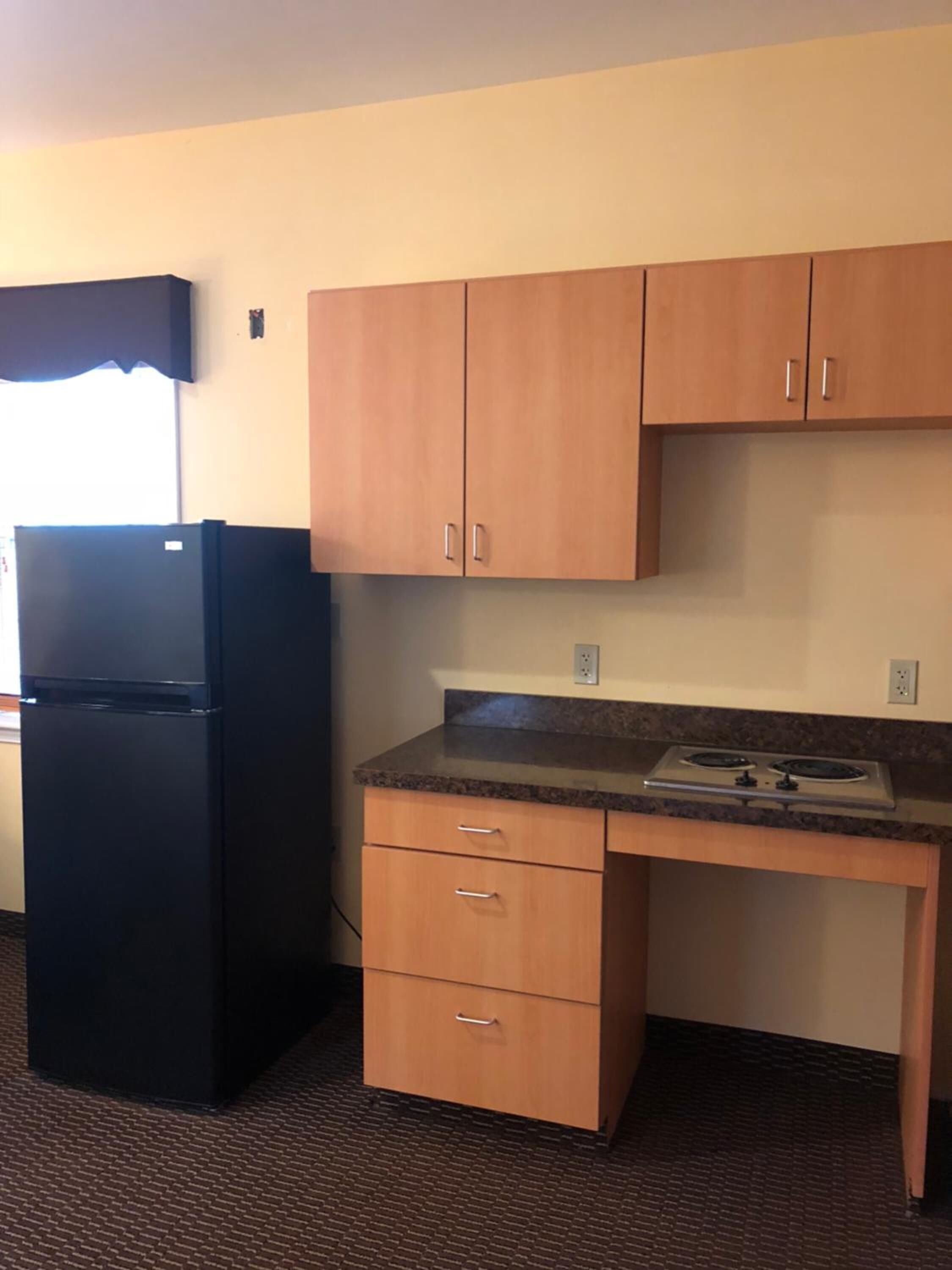 A compact kitchen with wooden cabinets, a black refrigerator, and a granite countertop.