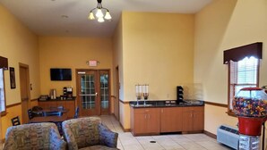 A room with two patterned armchairs, a kitchen area with wooden cabinets, a red gumball machine, and an exit sign. - Budget Inn Williamsport (Williamsport)